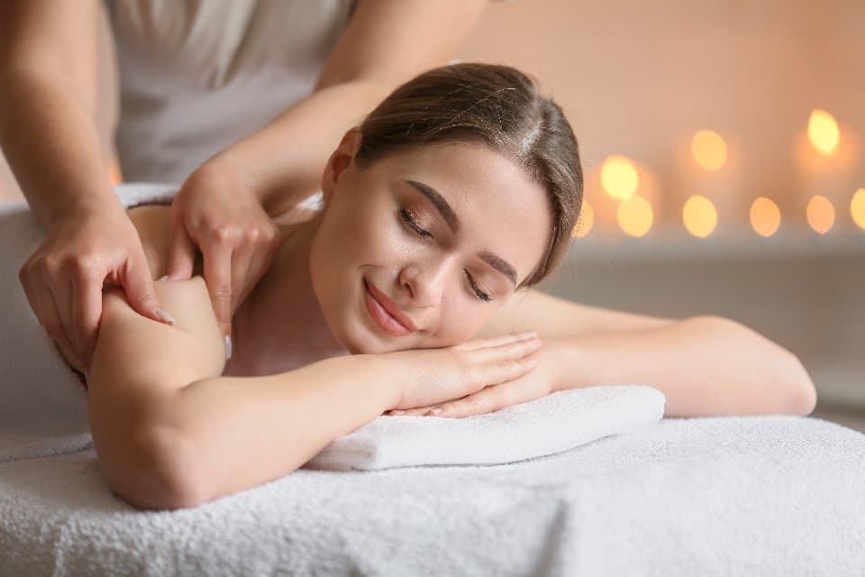 Sala de massagem em um spa com cama e toalhas brancas, iluminação indireta.